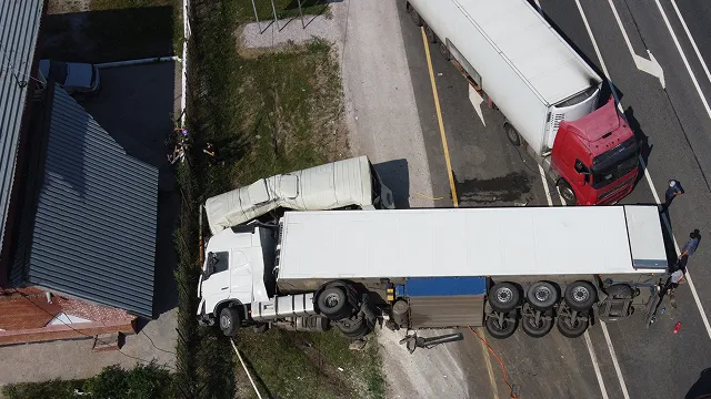 An aerial, top-down view of a traffic accident involving multiple semi-trucks blocking the roadway, with one white truck jackknifed across the lanes.